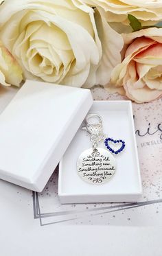 a white box with a blue beaded heart charm and some flowers on the table