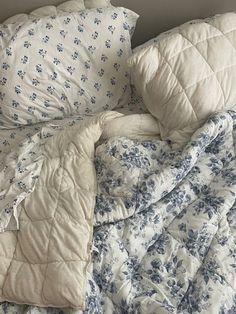 an unmade bed with blue and white flowers on the comforter, pillows and sheets