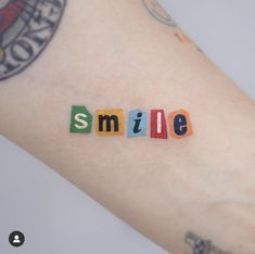 the word smile spelled out in small blocks on someone's arm with tattoos and piercings