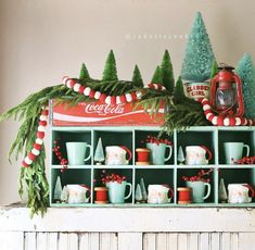 a shelf filled with cups and mugs sitting on top of a mantle covered in christmas decorations