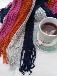 a cup of tea sits on a saucer next to a multicolored scarf