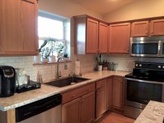 a kitchen with wooden cabinets and stainless steel appliances, including a dishwasher, stove, microwave, sink and window