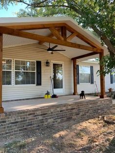 a dog is standing on the front porch under a pergolated roof with black shutters