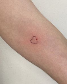 a small heart tattoo on the left forearm and arm, with a tiny red dot in the middle