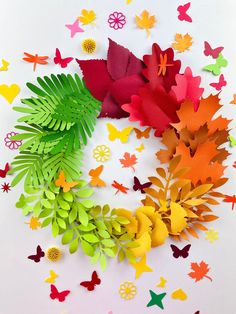 colorful paper butterflies and leaves arranged in a circle on a white surface with red, yellow, green, orange, and pink colors