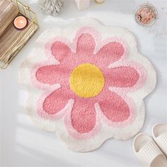 a pink and yellow flower shaped rug next to some shoes on a white table with candles