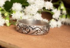 a silver ring sitting on top of a wooden table next to white flowers and greenery