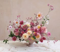 a vase filled with lots of flowers on top of a white cloth covered tablecloth