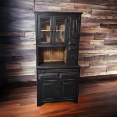 a black china cabinet sitting on top of a hard wood floor next to a wooden wall