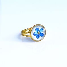 a ring with a blue flower on it sitting on a white surface, in front of a white background