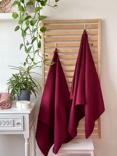 two red towels hanging on the wall next to a white table and potted plant