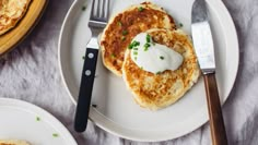 pancakes with sour cream and chives are on a plate next to a knife and fork