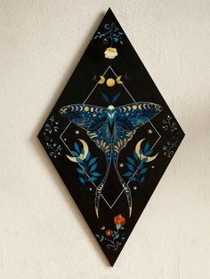 a decorative wall hanging with a blue butterfly on it's face and flowers in the background