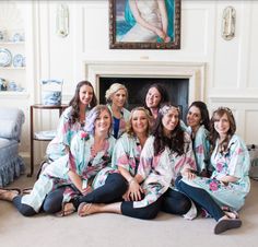 a group of women sitting next to each other in front of a fireplace wearing matching robes