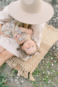 a woman holding a baby in her arms while sitting on a rug with a hat over her head