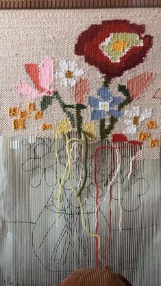 a vase filled with flowers sitting on top of a table next to a wall hanging