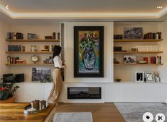 a woman standing in front of a painting on the wall next to a fire place