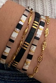 three different bracelets on someone's arm with gold chains and black and white beads