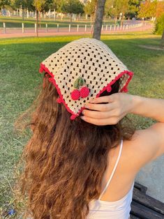 a woman sitting on top of a wooden bench wearing a crocheted strawberry hat