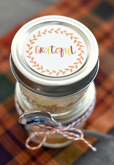 a jar filled with food sitting on top of a plaid tablecloth covered floor next to a metal spoon