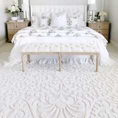 a white bed sitting in a bedroom next to two dressers and a large mirror