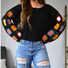 a woman wearing ripped jeans and a black sweater with colorful crochet trims