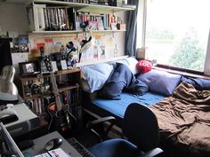 a bedroom with a bed, desk and guitar in the corner next to a window