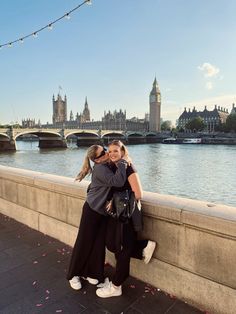 two women hugging each other on the side of a bridge over water with buildings in the background