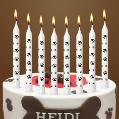 a dog themed birthday cake with white candles and paw prints on the candle holders,