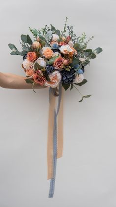 a bridal bouquet is being held up by someone's hand with the ribbon tied around it