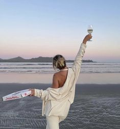 a woman standing on top of a beach holding a wine glass in one hand and a bottle in the other