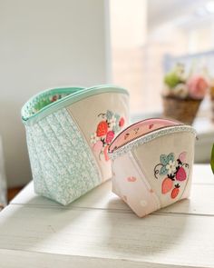 two small pouch bags sitting on top of a table next to an apple and flower pot