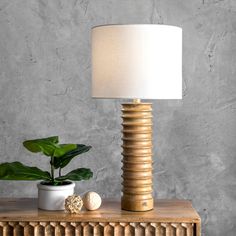 a table lamp sitting on top of a wooden dresser next to a potted plant