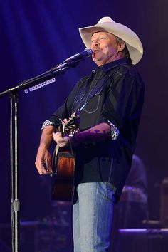 a man wearing a cowboy hat and holding a guitar in front of a microphone on stage