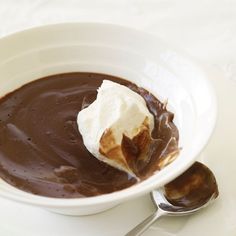 a white bowl filled with chocolate and whipped cream on top of a plate next to a spoon