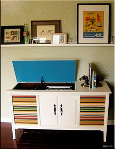 a record player sitting on top of a white cabinet next to a wall with pictures above it