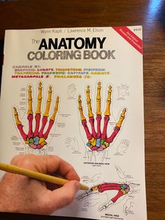 the anatomy coloring book is being held by a person's hand with a pencil