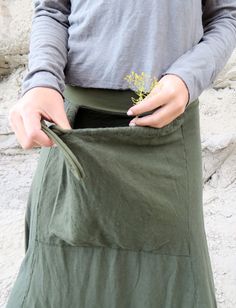 a woman is holding her pocket open to show the inside of her skirt, which has a small plant growing out of it