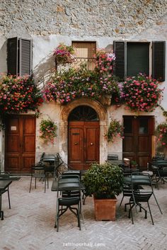 an outdoor cafe with tables and chairs covered in flowers, next to a stone building