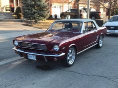 an old mustang is parked on the side of the road in front of another car