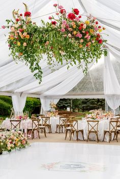 the inside of a tent with tables, chairs and flowers hanging from it's ceiling