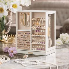 a white box filled with lots of jewelry on top of a table next to flowers