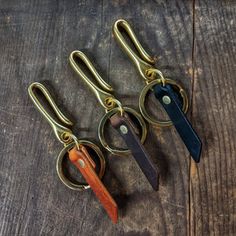 three pairs of scissors are sitting on a wooden table with metal hooks and leather handles