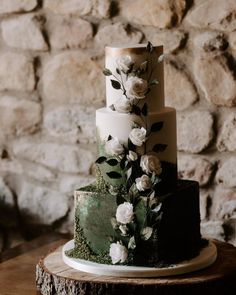 a three tiered cake with white flowers and greenery sits on a tree stump