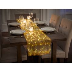 a long table with white plates and glasses on it is decorated with yellow fairy lights