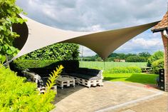 an outdoor patio with furniture under a large shade sail over it's back yard