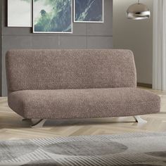 a brown couch sitting on top of a wooden floor next to a wall with pictures above it