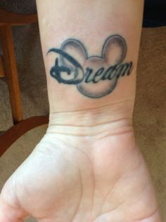 a small wrist tattoo with the word dream on it's left arm and mickey mouse head