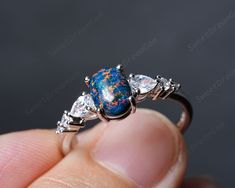 a person is holding a ring with an opal and diamonds on it