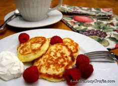 two pancakes with raspberries and whipped cream on a plate next to a cup of coffee